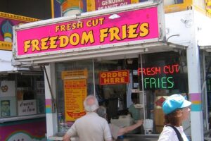 Pommesbude, über der ein großes pinkes Schild hängt, auf dem in gelber Schrrift steht: "Fresh Cut. Freedom Fries"