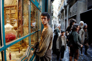 Filmausschnitt: ein Mann steht vor einem Schaufenster, das hell erleuchtet ist. Die Straße ist dunkel. Der Mann schaut Richtung Kamera