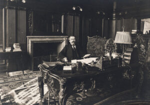 Aristide Briand hinter einem massiven Schreibtisch sitzend, im Hintergrund ein Kamin