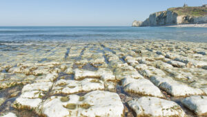 Die Klippen von Étretat bei Ebbe, vorne Steine, hinten Wasser und Klippen