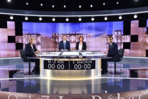 TV-Duell zwischen Le Pen und Macron, beide sitzen sich an einem großen Tisch gegenüber, in der Mitte zwei Moderator*innen