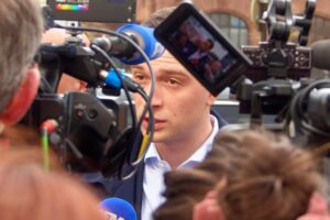 Im Vordergrund Kameras, im Hintergrund das Gesicht von Jordan Bardella