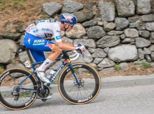 Ein Fahrer mit weißem Trikot und blauer Hose auf einem Fahrrad bei einem Anstieg