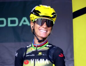 Frau mit gelbem Helm, Radbrille und schwarzem Trikot, lächelnd