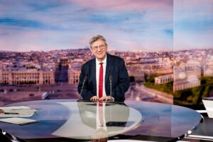 Mann mit Brille, Anzug und Krawatte an einem Tisch in einem Fernsehstudio