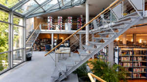 Im Vordergrund eine Treppe auf einer offenen Galerie, im Hintergrund Bücherregale
