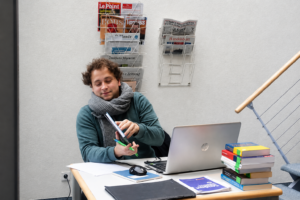 Ein junger Mann an einem kleinen Tisch mit aufgeklapptem Laptop und einem Bücherstapel