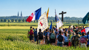 Große Wiese, auf der junge Menschen mit Flaggen und einem großen Kreuz laufen, von hinten abgebildet